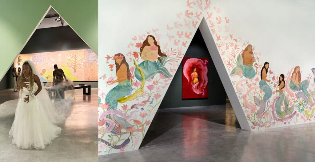 A woman in a white gown stands before an art installation with a triangular entrance, pastel murals of mermaids and sea creatures, and a vivid red portrait visible through the opening at Miami Art Week 2025. Other visitors explore the gallery inside.