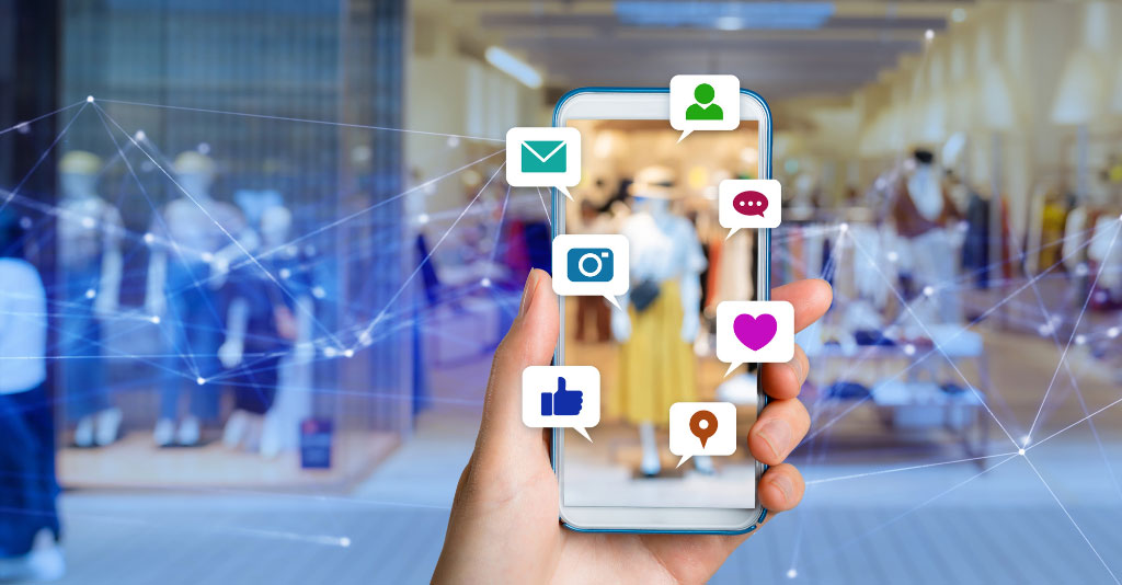 Image of person holding a phone with icons of social media apps in bubbles, over a background of a clothing store.