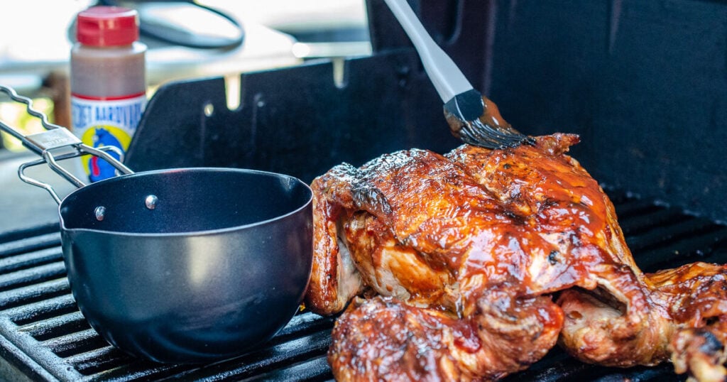 image of opened grill with whole chiken and bowl of sauce. A brush is placing sauce on chicken