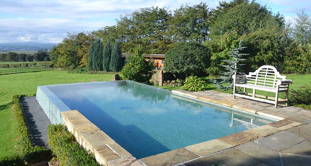 Piscine sur-mesure à débordement dans un jardin avec beaucoup de verdure.