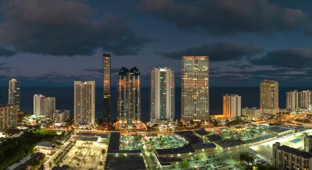 Vista aérea nocturna de rascacielos iluminados en Miami, símbolo de arquitectura moderna, dinamismo urbano y desarrollo sostenible.