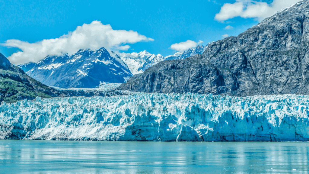 Majestic glacier flowing between snow-capped mountains in Alaska.