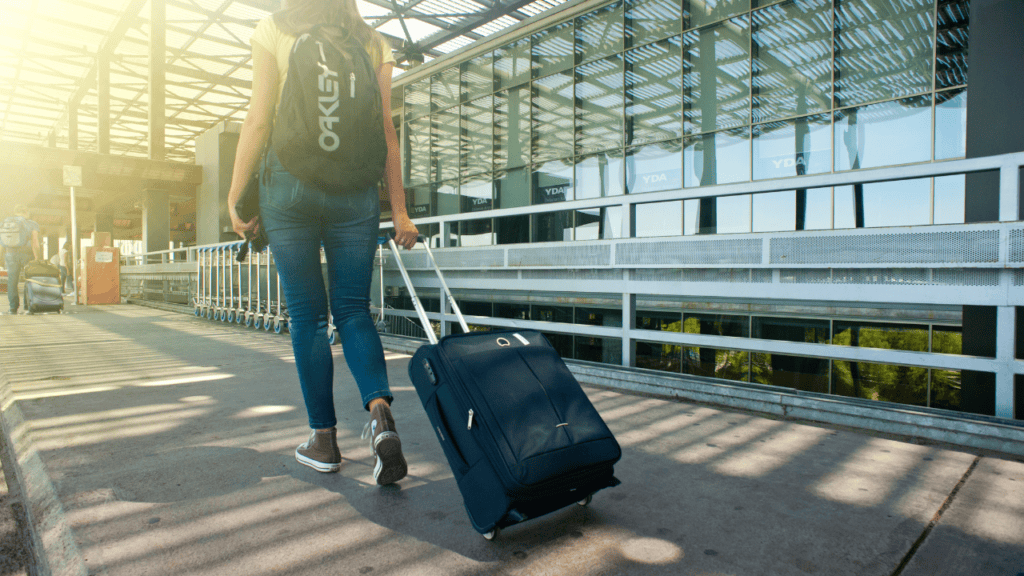 Woman with rolling suitcase at airport terminal, travel tips for a smooth vacation.