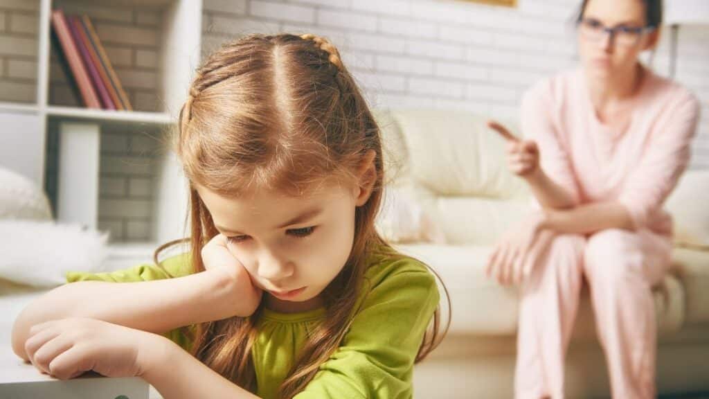Kind sitzt betrübt da, Mutter hat den Zeigefinger erhoben, sitzt weiter hinten. Denkt das Kind vielleicht: Ich bin falsch