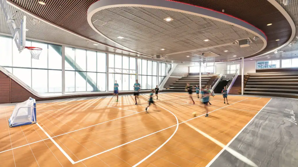 innenansicht des sportbereichs auf der mein schiff 1 mit kindern, die fußball spielen. hell erleuchteter raum mit großen fenstern und holzdetails.