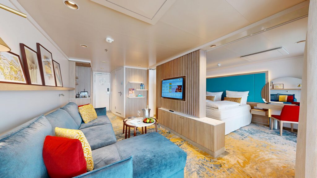 ein moderne suite mit einem gemütlichen wohnzimmerbereich, blauen sofas, einem fernseher, einem doppelbett und einem schreibtisch. stilvolle dekoration und angenehme farben schaffen eine einladende atmosphäre.