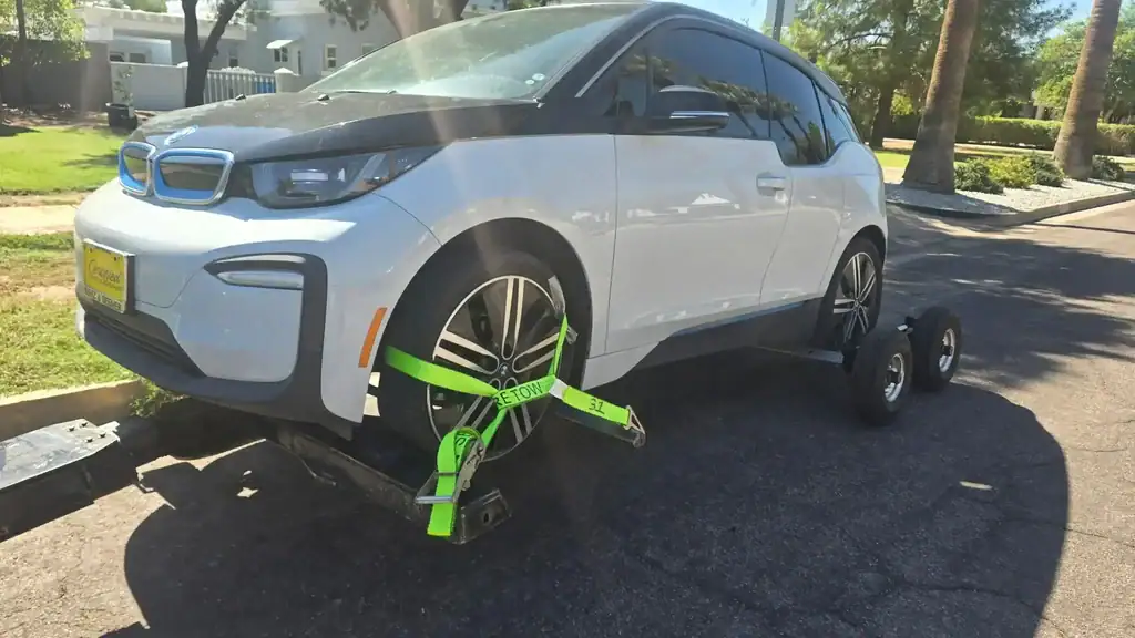 BMW i3 being carefully moved from a tight parking space in Phoenix using a wheel-lift with tow dollies