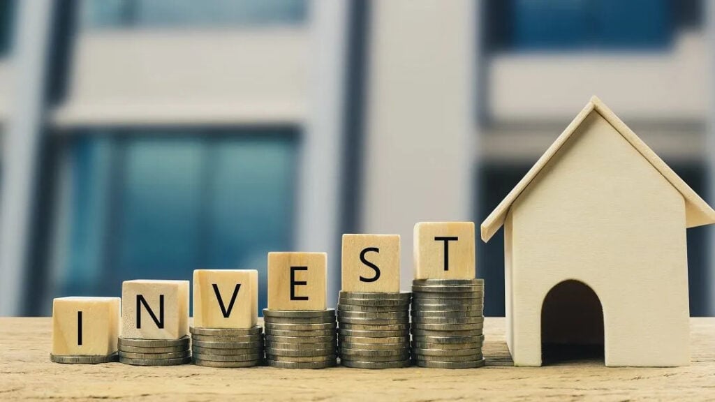 Real estate investment concept with INVEST blocks, coin stacks and house model