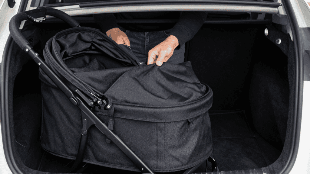 Placing a compact foldable travel dog stroller into a car trunk.