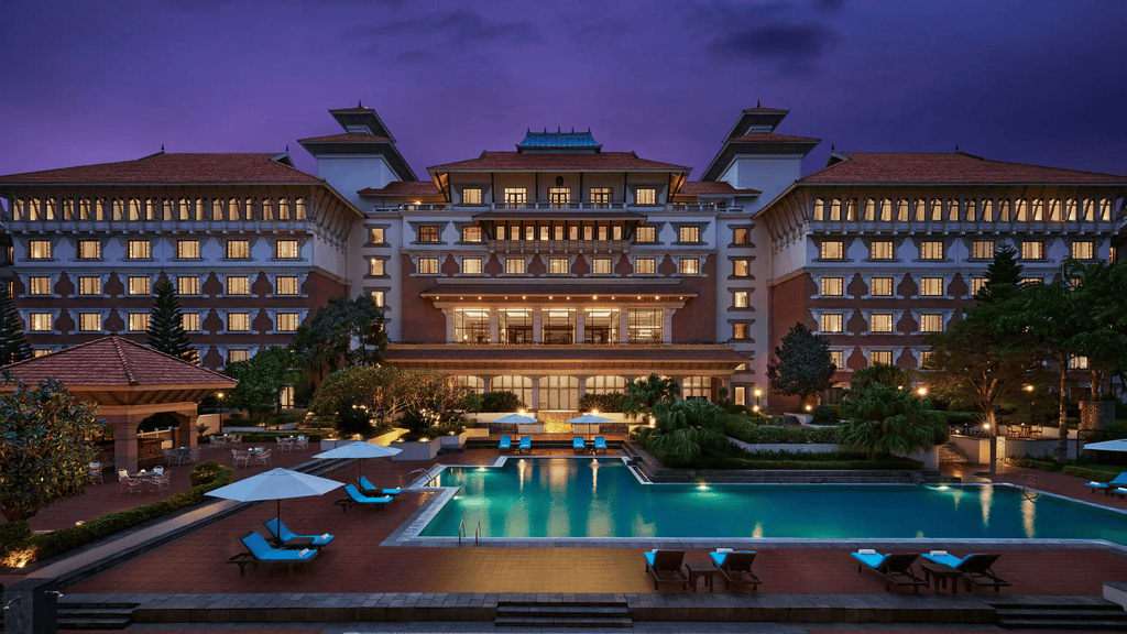 Exterior evening view of a sprawling 5-star luxury resort hotel with an illuminated swimming pool. It illustrates ongoing development in the high-end hospitality real estate market.