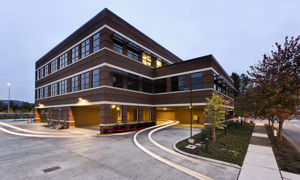1700 Nw Gilman Blvd - Brick office building at twilight with illuminated windows and driveway lights