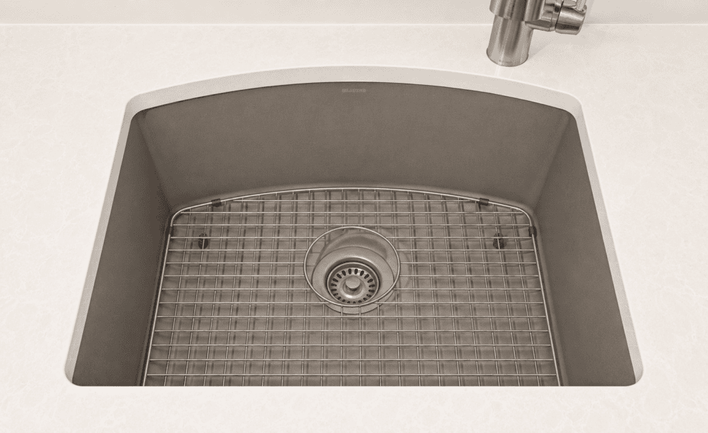Top down view of a beige toned kitchen sink with a metal wire rack drainer over the drain and a faucet visible in the corner