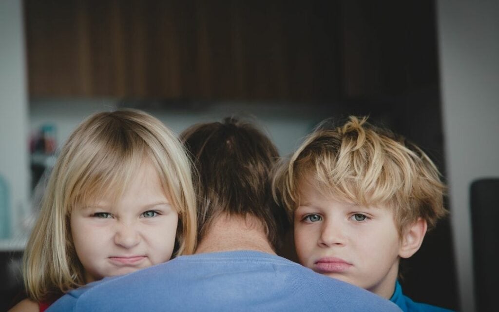 Genervt von den Kindern, Vater umarmt seine beiden Kinder, die Kinder sehen genervt aus