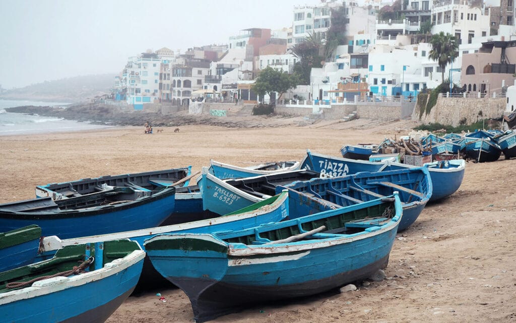 blue fisher boats and white houses in taghazout bay surf village, southern morocco