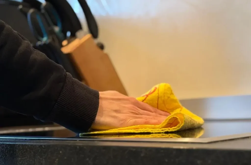 Hand wischt Küchenarbeitsfläche mit Reinigungstuch – Symbol für gründliche Unterhaltsreinigung im Haushalt.