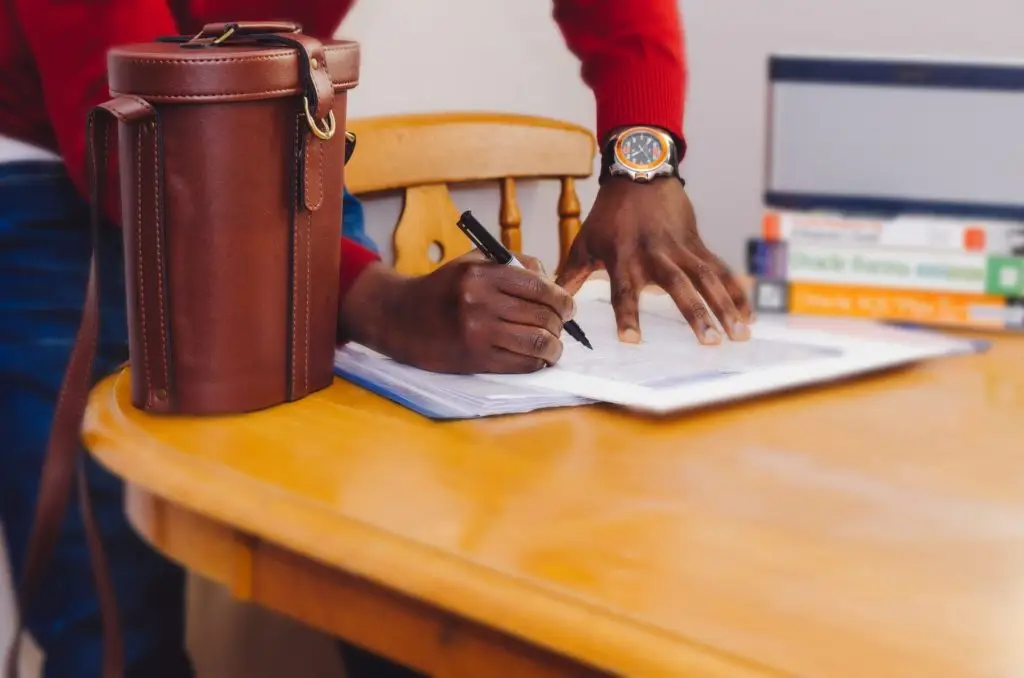 man in red sweater with really nice watch signing a contract with an attache on a table