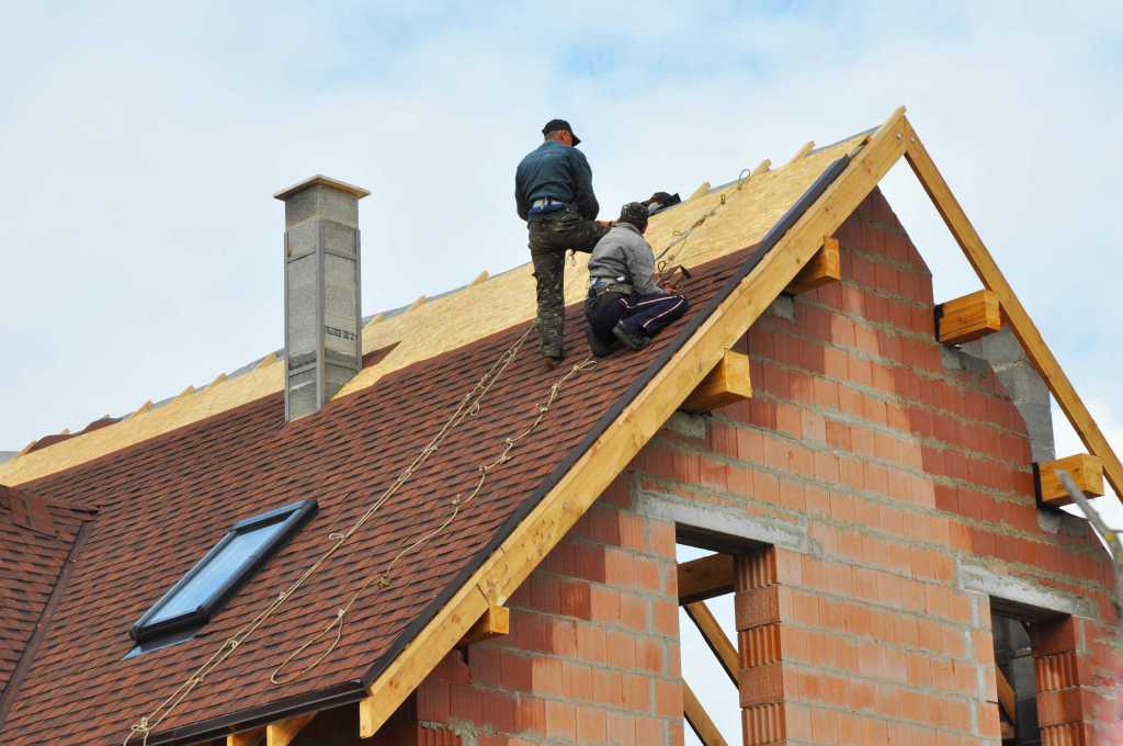 Two men laying down red shingles on a roof of a house in Florida.
