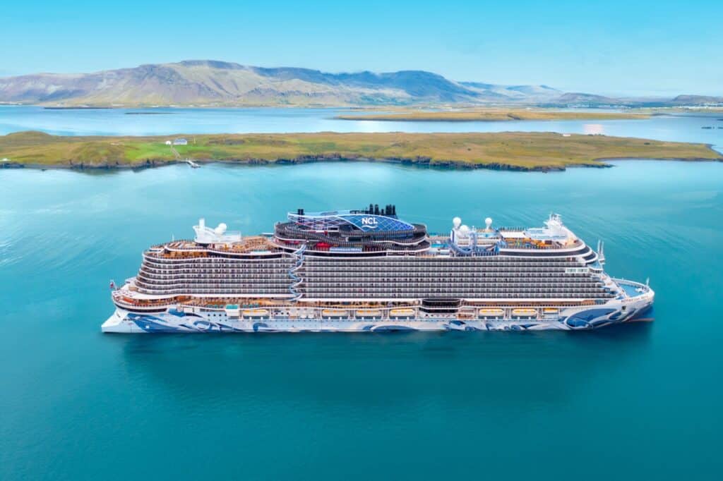 Elegant cruise ship sailing through calm waters with scenic landscape backdrop.
