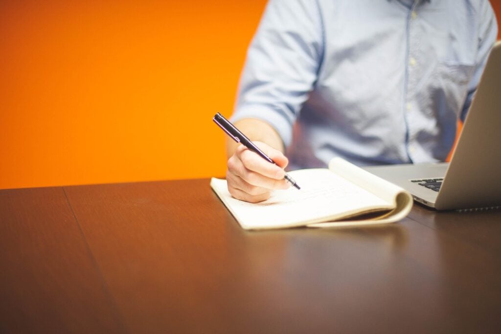 Professional on laptop taking notes on a table behind an orange background