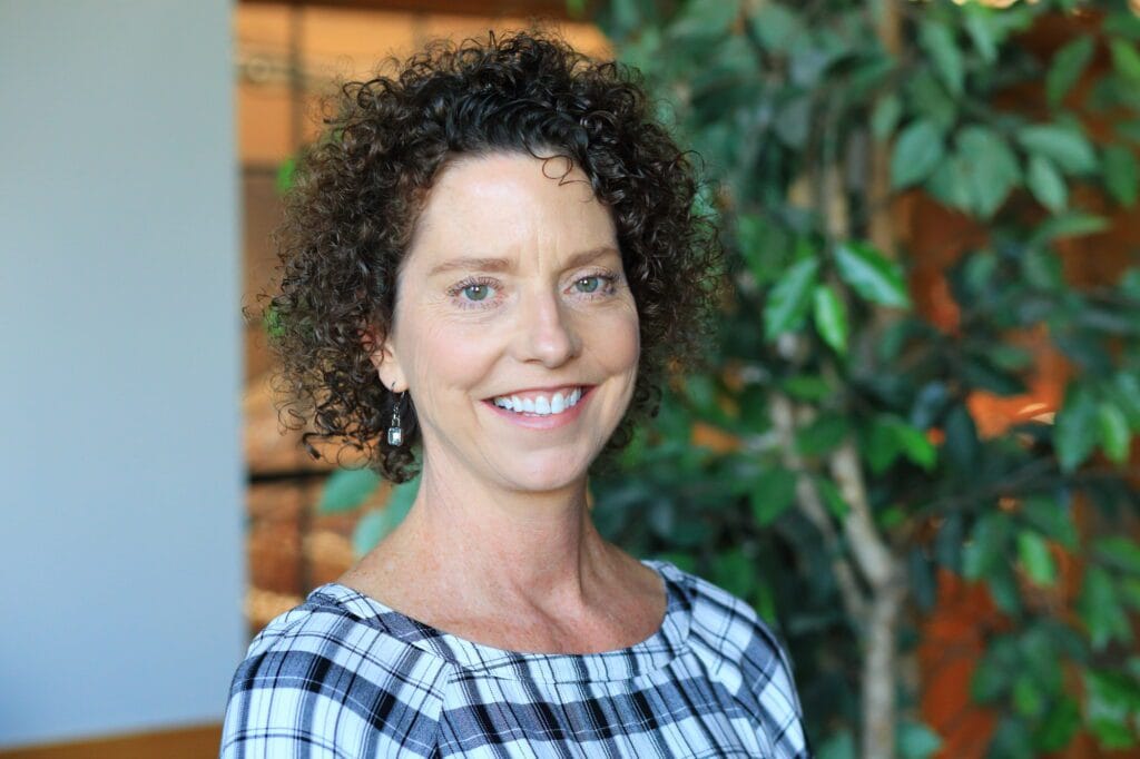 A woman with curly hair smiling indoors.