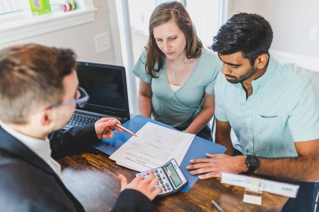 A Man in a Black suit with a Calculator Explaining Paperwork to a Couple
