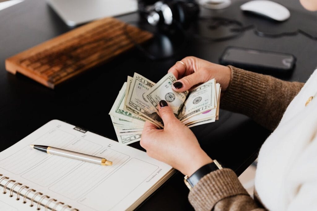 Person Counting Cash Infront of a Grey Table and a Notebook
