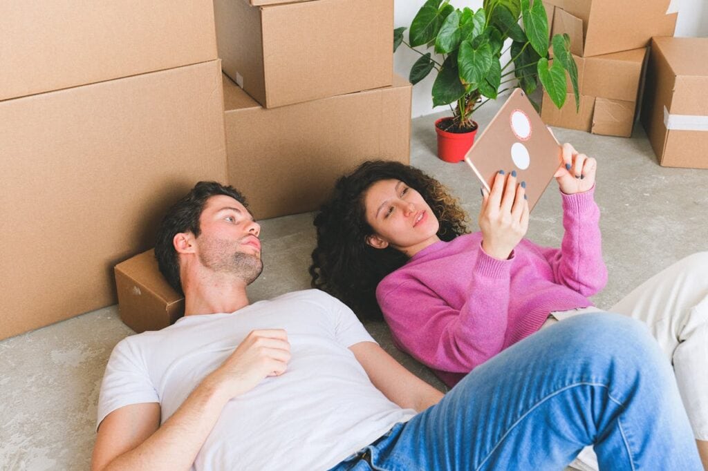 A Couple Lying on the Floor Looking at a Tablet with Boxes on the Background