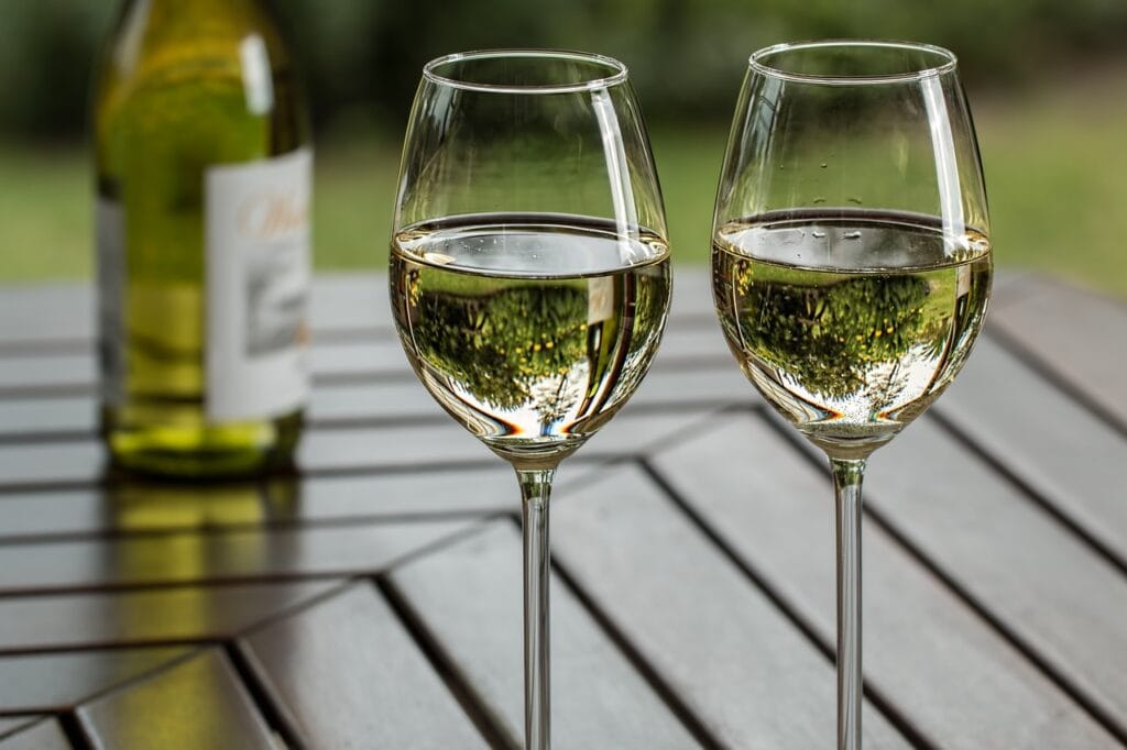 Two clean wine glasses half full sitting on wooden table outdoors.
