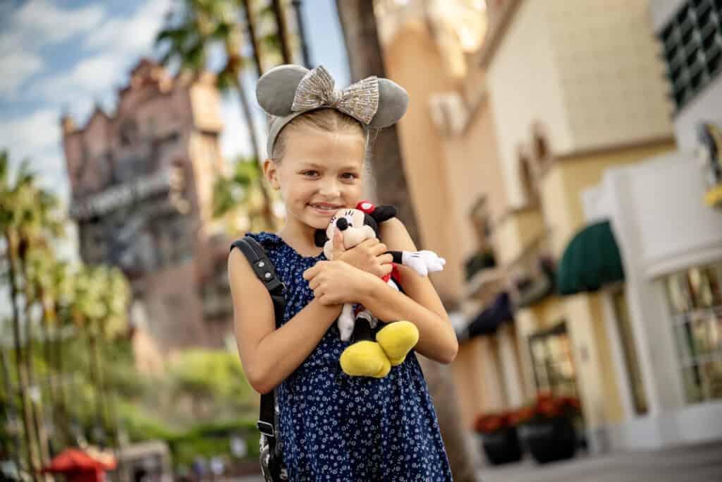 Cute young girl holding Minnie Mouse plush toy at Disney theme park, on vacation, traveling with children, family fun activities in Orlando Florida.