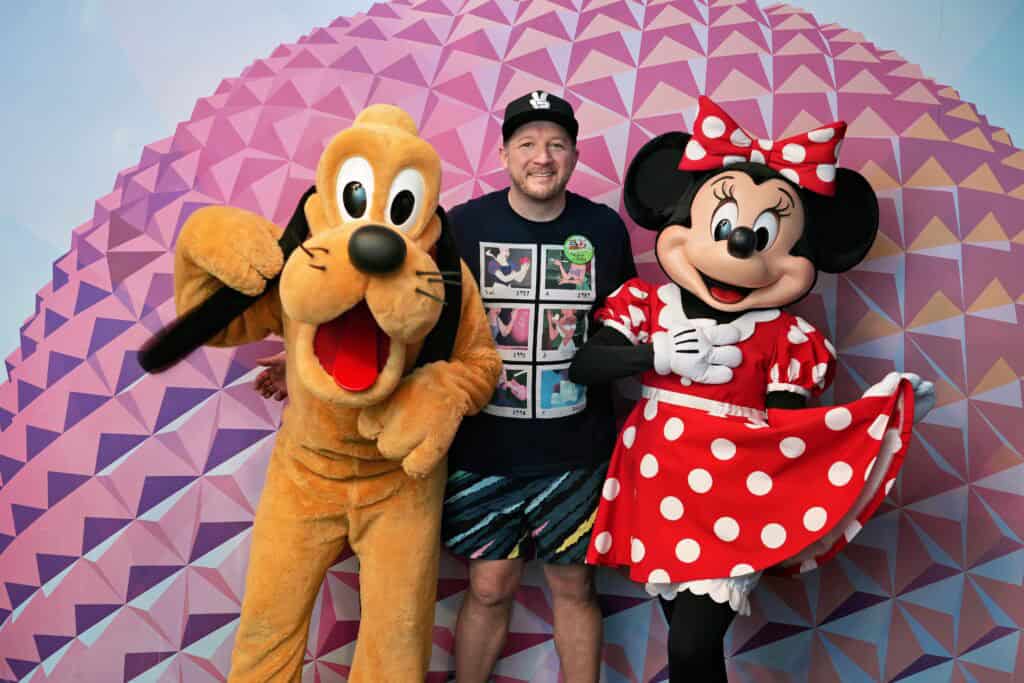 Disney characters Mickey Mouse and Pluto with a guest at a theme park.