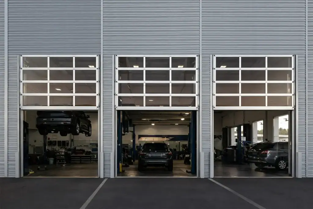 High-lift full-view sectional doors operating in an automotive service and maintenance bay, providing essential ceiling clearance for car hoists and maximizing operational efficiency.