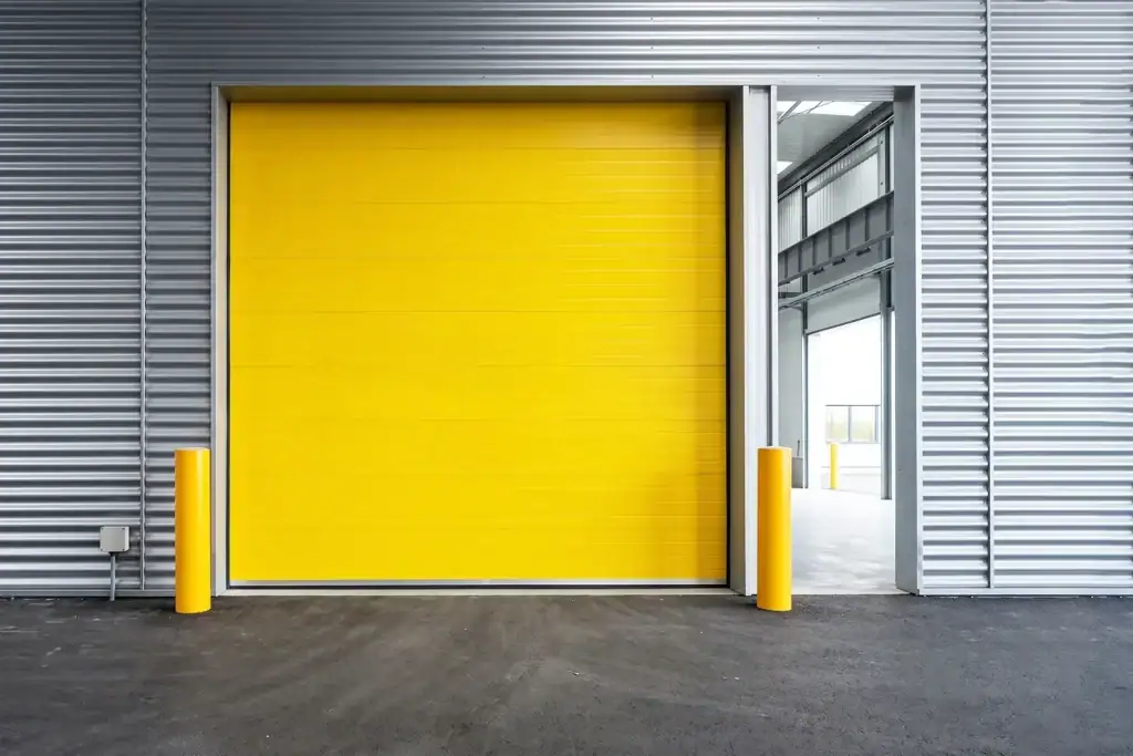 Heavy-duty yellow industrial sectional door installed in a heavy manufacturing plant, reinforced with external wind struts to withstand extreme pressure differences in massive production halls.