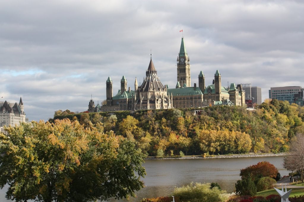 A collection of Gothic Revival buildings on a tree-lined hill over-looking a river on a cloudy day