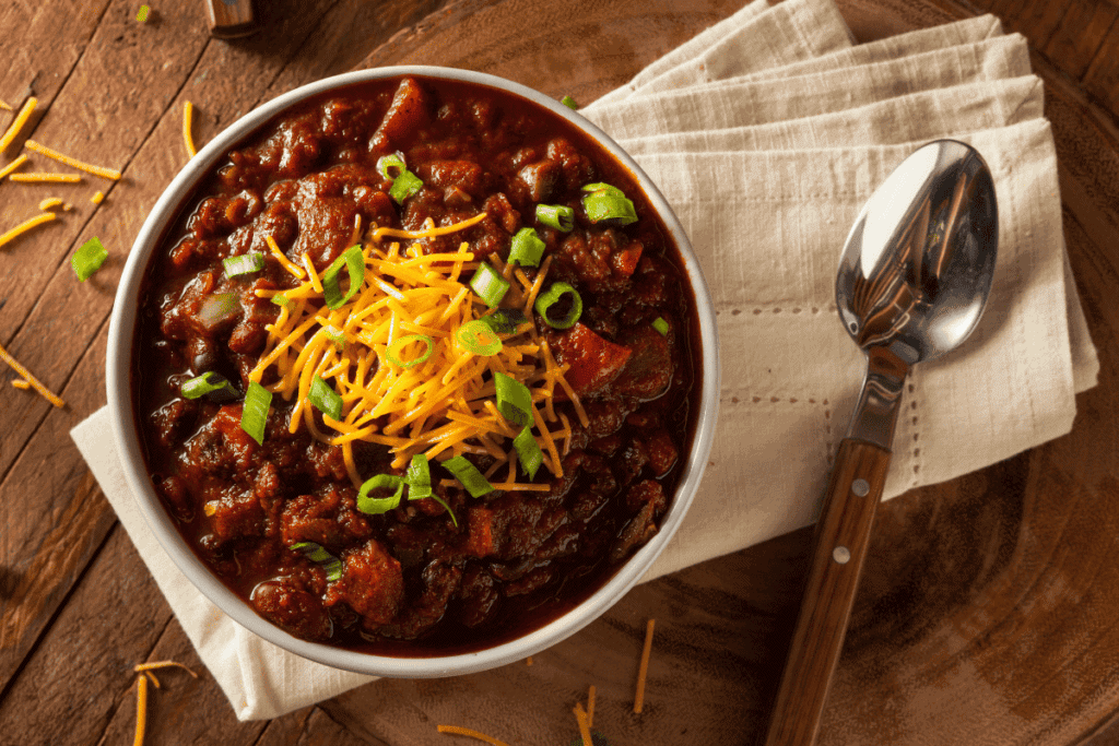 A bowl of chunky chilli topped with cheese and green onions.