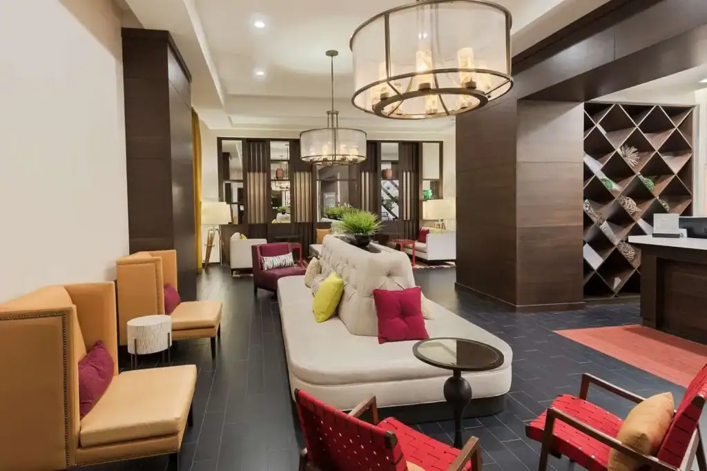 Modern hotel lobby design with comfortable lounge seating, decorative pendant lighting, dark wood accents, and a reception desk.
