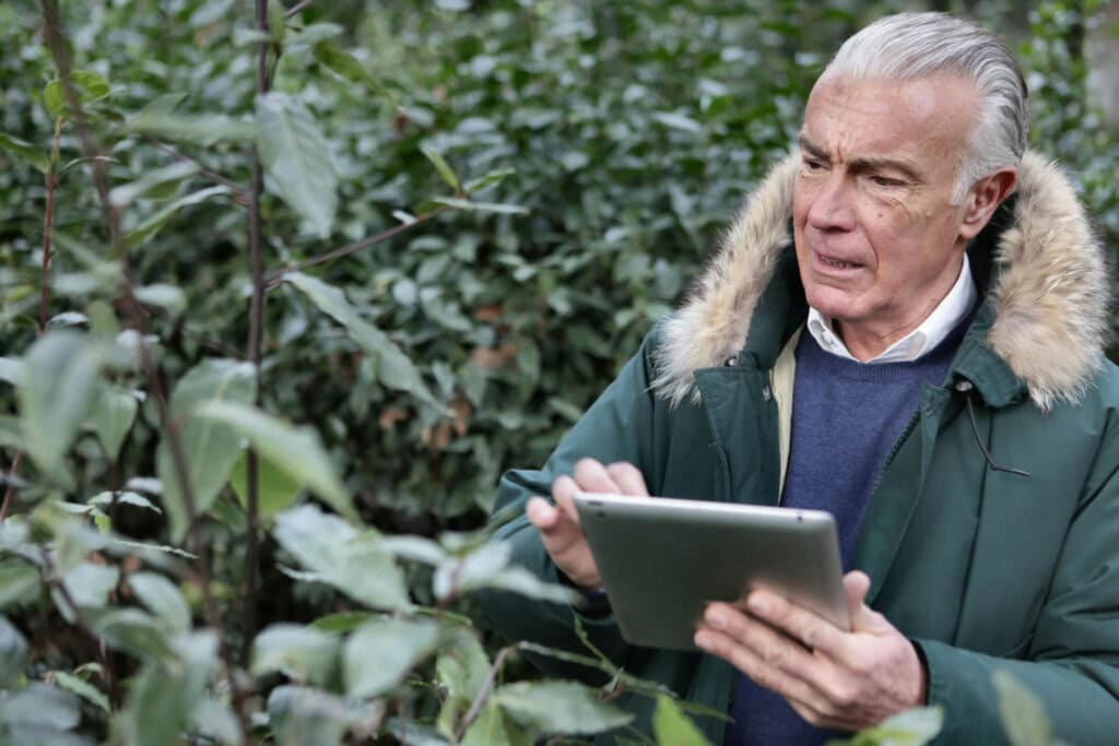 Ein älterer Mann in einem Garten mit einem IPad in der Hand.
