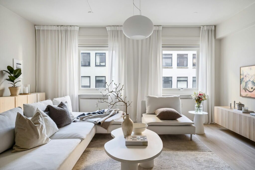 Bright Scandinavian living room with modern minimalist white sofas, sheer curtains, and natural light.