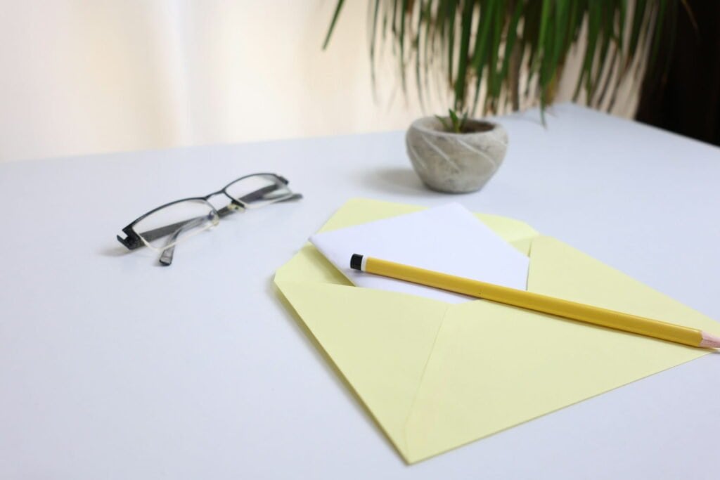 Envelope with a yellow pencil, glasses, and a small potted plant on a white desk for FashionCressta contact page