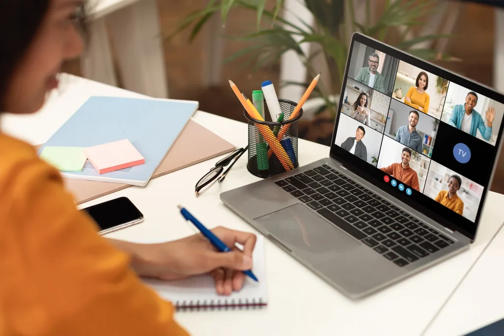 Person taking notes during a virtual meeting or online class displayed on a laptop screen with multiple participants.