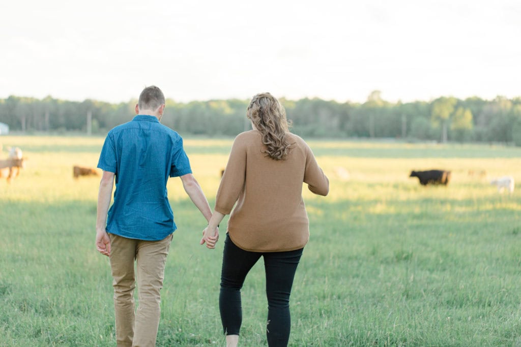 Cows during Engagement Session - Poses during Engagement Session Sunset - Natural Posing for Photo Session - Couples Photo Session Fun - Fun on the Farm - Farm Engagement Session - Blue and Brown Engagement Session Inspiration - Natural Engagement Session Posing - Ideas for what to wear for Engagement Photography, Modern Engagement Session Inspiration Wardrobe Ideas. Unsure of what to wear for your engagement photos, we've got you! Romantic brown with black leggings for Summer Engagement in Almonte. Grey Loft Studio is Ottawa's Wedding and Engagement Photographer for Real couples, showcasing photos that are modern, bright, and fun.