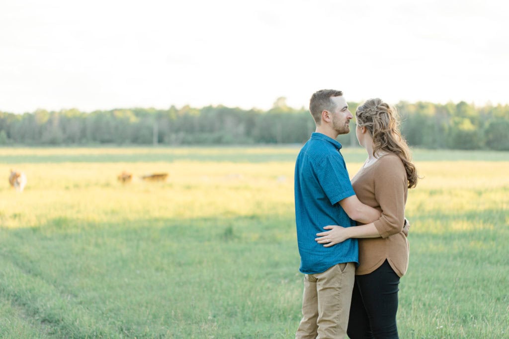 Cows during Engagement Session - Poses during Engagement Session Sunset - Natural Posing for Photo Session - Couples Photo Session Fun - Fun on the Farm - Farm Engagement Session - Blue and Brown Engagement Session Inspiration - Natural Engagement Session Posing - Ideas for what to wear for Engagement Photography, Modern Engagement Session Inspiration Wardrobe Ideas. Unsure of what to wear for your engagement photos, we've got you! Romantic brown with black leggings for Summer Engagement in Almonte. Grey Loft Studio is Ottawa's Wedding and Engagement Photographer for Real couples, showcasing photos that are modern, bright, and fun.