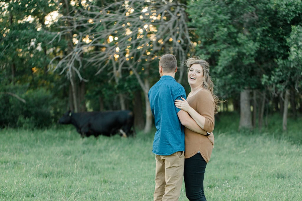 Cow Photobomb - Cows during Engagement Session - Poses during Engagement Session Sunset - Natural Posing for Photo Session - Couples Photo Session Fun - Fun on the Farm - Farm Engagement Session - Blue and Brown Engagement Session Inspiration - Natural Engagement Session Posing - Ideas for what to wear for Engagement Photography, Modern Engagement Session Inspiration Wardrobe Ideas. Unsure of what to wear for your engagement photos, we've got you! Romantic brown with black leggings for Summer Engagement in Almonte. Grey Loft Studio is Ottawa's Wedding and Engagement Photographer for Real couples, showcasing photos that are modern, bright, and fun.