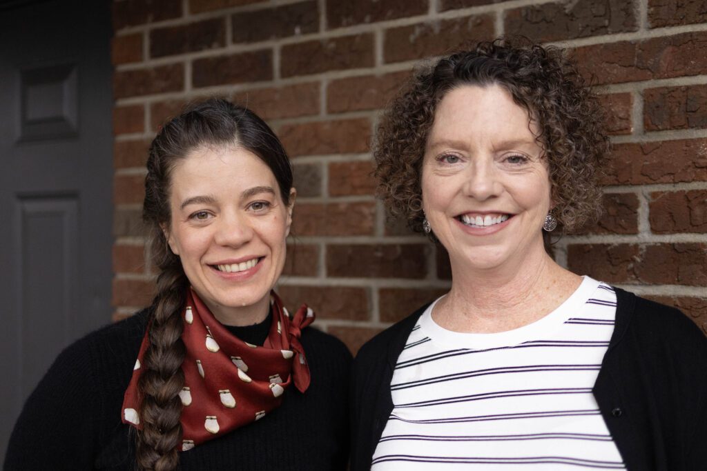 Two women smiling in front of bricks.