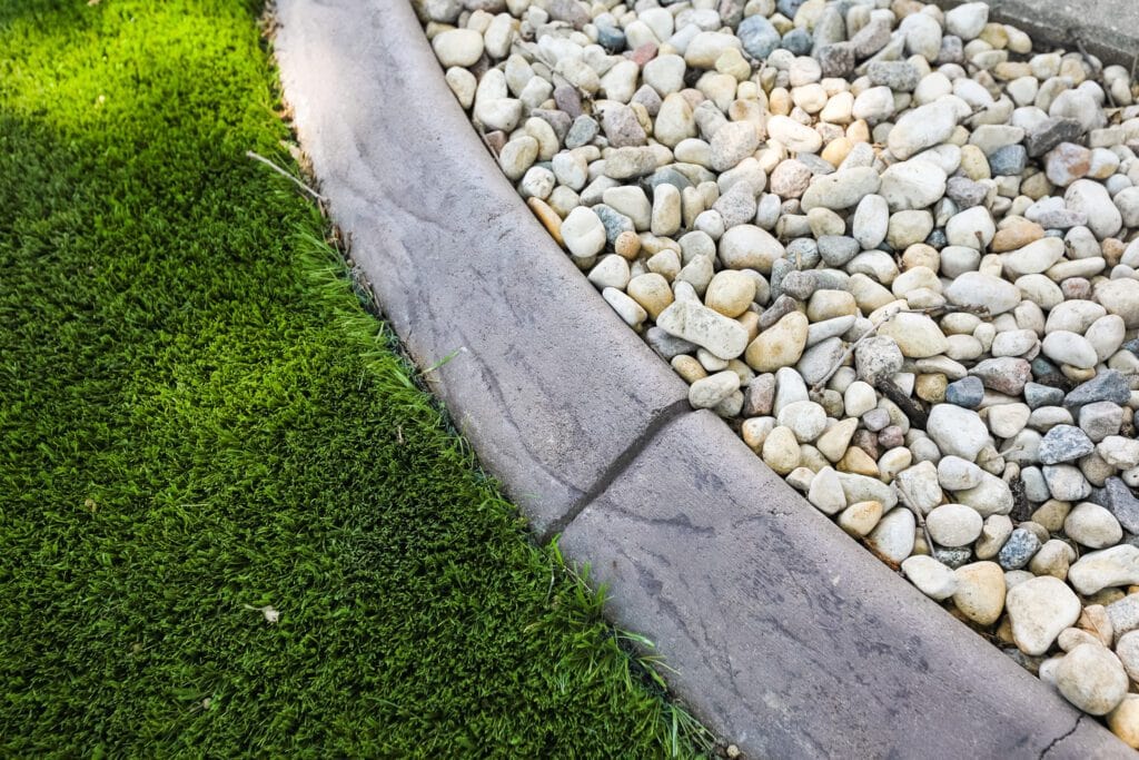 Close-up of garden edging with decorative white river rocks and green grass border.