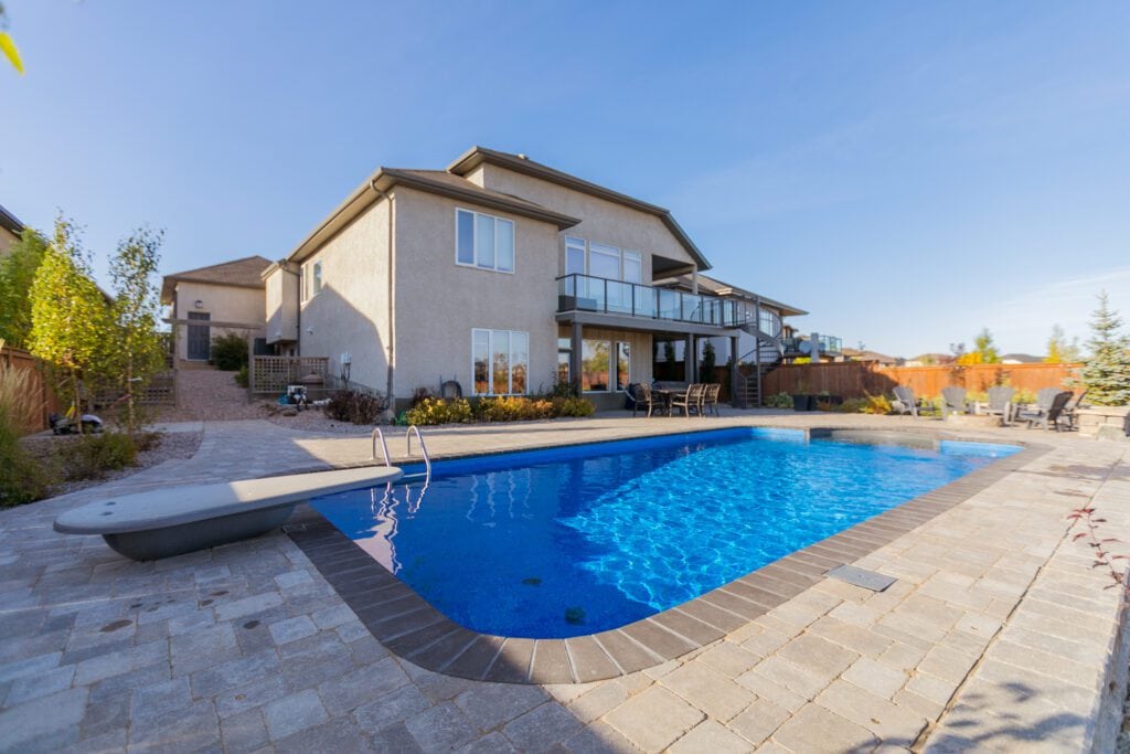 Inground fiberglass pool in residential backyard with patio and landscaping design.