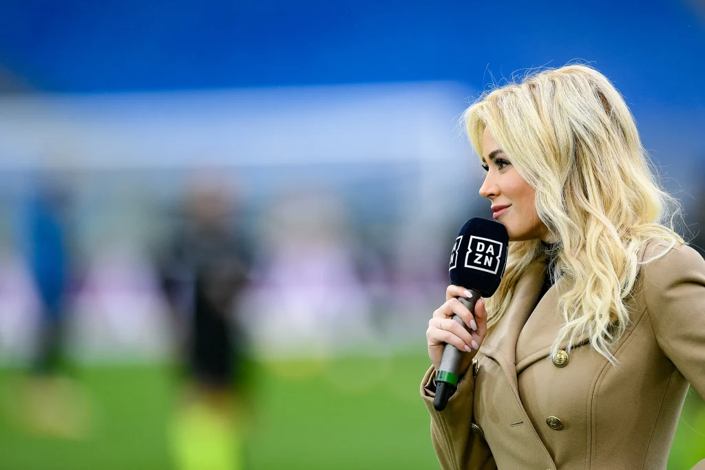 Blonde sports presenter holding a branded microphone windshield during live broadcast interview