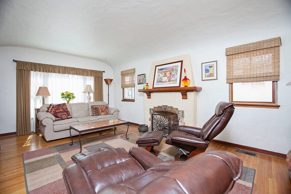 Craftsman-style living room at 3317-3319 Boundary Street in North Park featuring a decorative fireplace with a wood mantel, leather recliner chairs with ottomans, and a neutral sofa on a multi-colored geometric area rug.