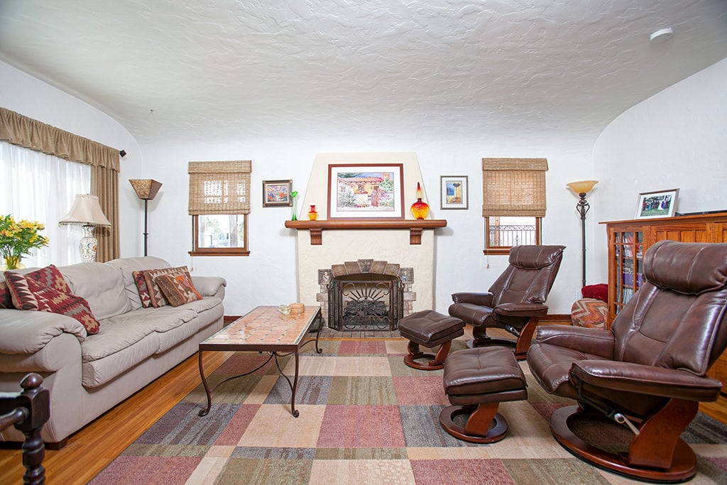 Craftsman-style living room at 3317-3319 Boundary Street in North Park featuring a decorative fireplace with a wood mantel, leather recliner chairs with ottomans, and a neutral sofa on a multi-colored geometric area rug.