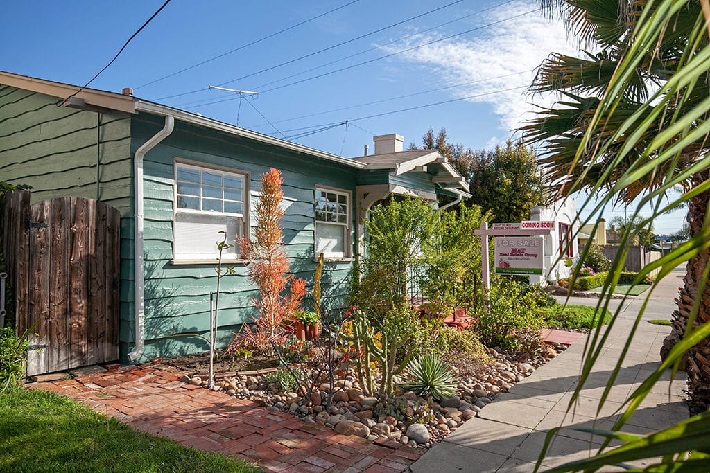Side view of a teal North Park bungalow at 3216 Landis St featuring a "For Sale" sign, a rustic wood gate, and a xeriscaped front yard with succulents and river rock.