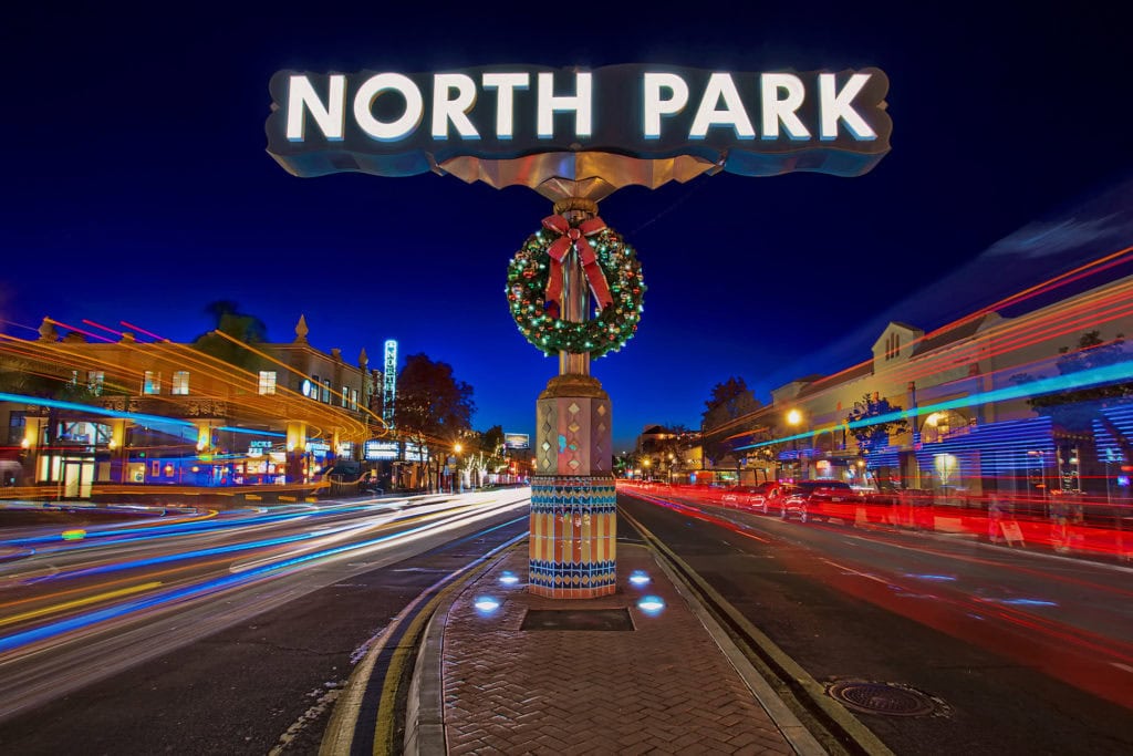 Illuminated North Park neighborhood sign at night with a holiday wreath and long-exposure light trails from passing traffic.